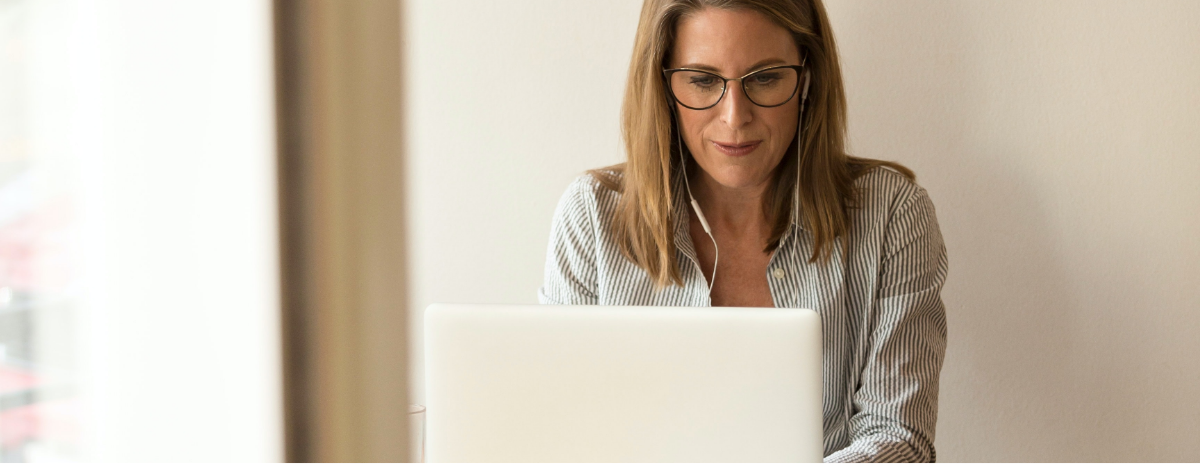 woman with glasses and headphones working on a laptop