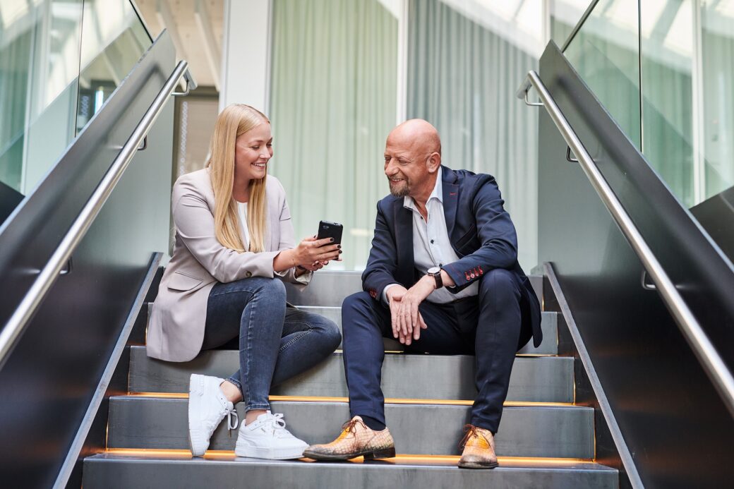 d.velop employees are sitting on the stairs with a smartphone